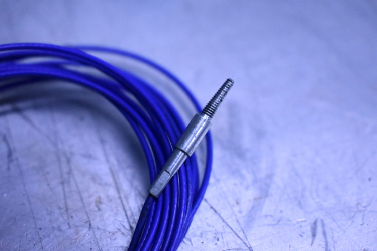 Close-up of a metallic connector partially attached to a coil of blue wire, set against a light gray textured surface.