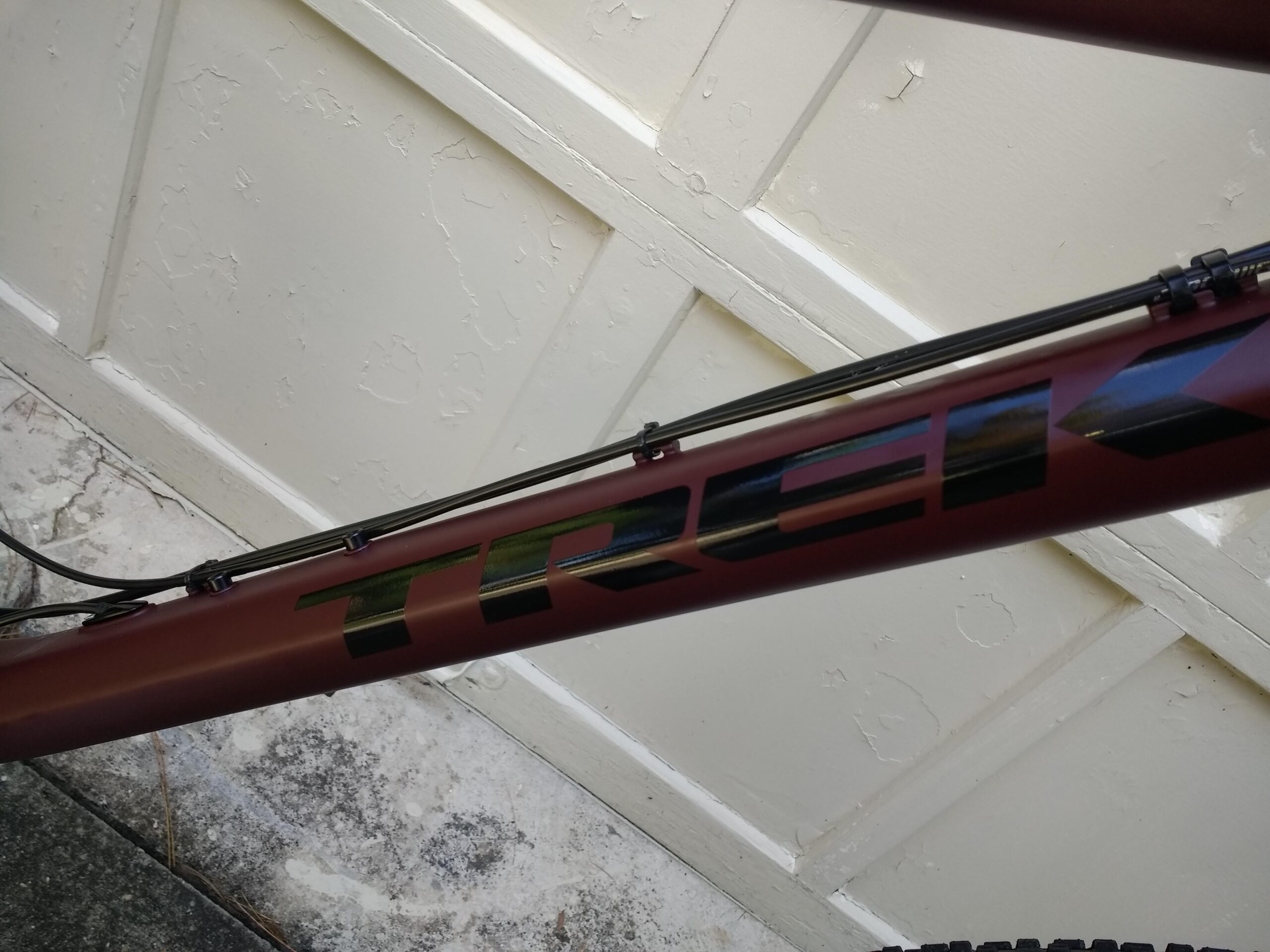 Trek Stache 7: A close-up view of a Trek bicycle frame, featuring a matte maroon finish with black lettering. The image captures the details of the frame, including cable routing and texture, against a light-colored textured background.