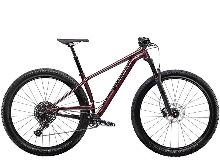 Trek Stache 7: A sleek, maroon mountain bike with a lightweight frame, featuring wide, knobby tires for enhanced traction. The bike is equipped with a front suspension fork, and its handlebar is designed for a comfortable grip. The image showcases the bike in a side view, highlighting its modern design and sporty aesthetics.