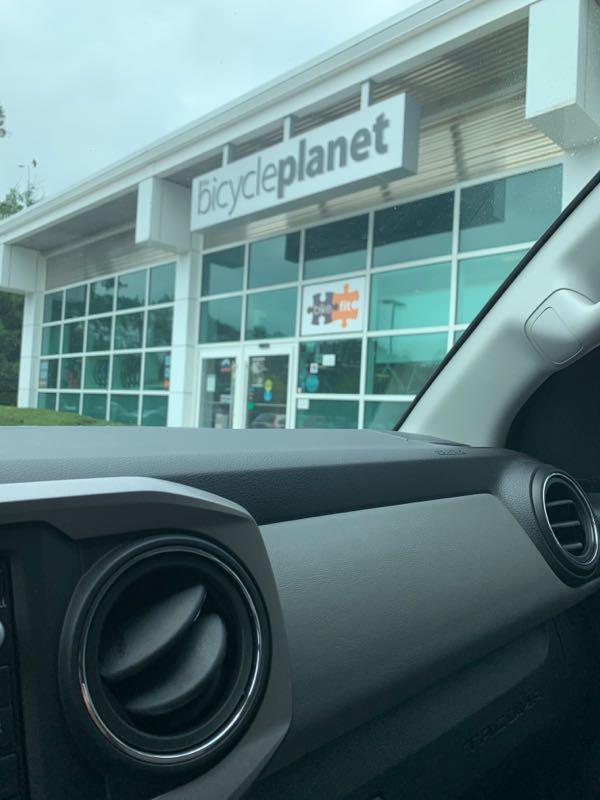 A view from inside a vehicle showing the exterior of a store named "bicycleplanet," featuring large glass windows and a modern design. The image captures the store