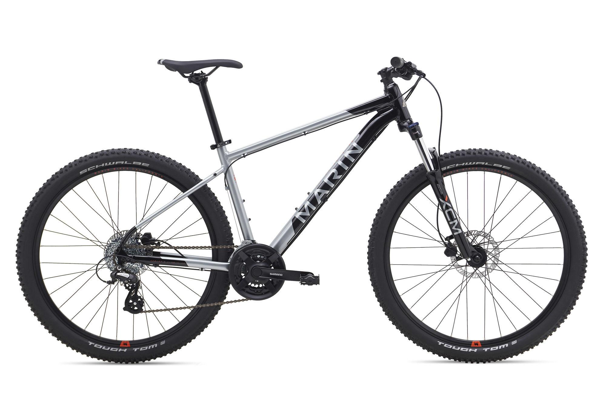 Marin Bobcat Trail: Alt tag: A silver and black mountain bike with wide tires, front suspension, and a Shimano drivetrain. The bike is positioned on a plain white background, showcasing its sleek design and features.