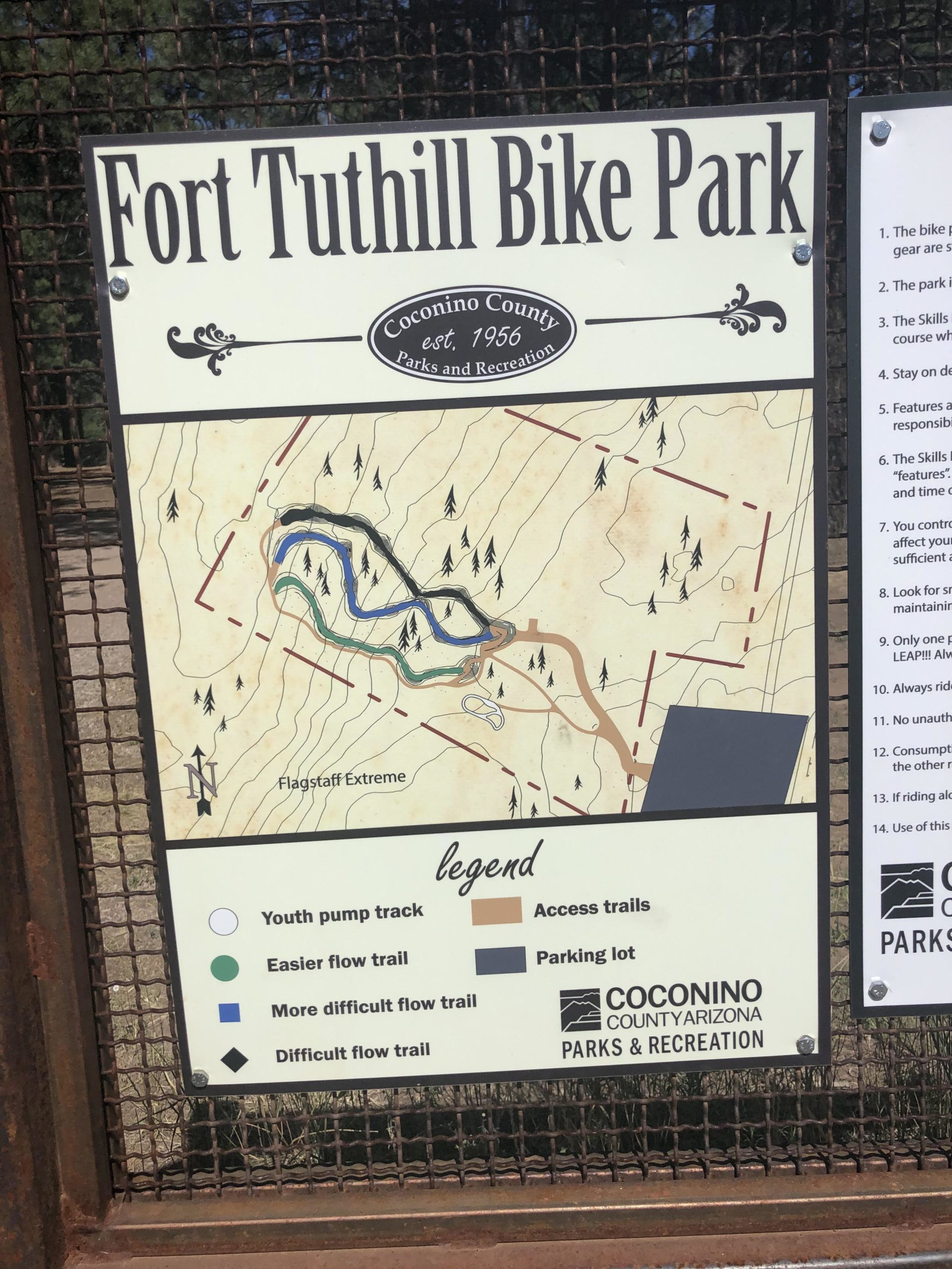 Sign for Fort Tuthill Bike Park, featuring a map that outlines various bike trails, including youth pump tracks and different difficulty levels for flow trails. The sign is part of Coconino County Parks and Recreation, established in 1956, and includes a legend for trail types and access points. Soldiers Loop / Fairgrounds trails mountain bike trail.