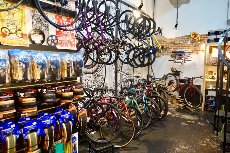 A vibrant bicycle shop interior featuring various types of bicycles on display. The walls are adorned with colorful posters and murals, while shelves showcase bike accessories, including tires and grips. A mix of road and mountain bikes in different colors line the floor, creating an inviting atmosphere for cycling enthusiasts.