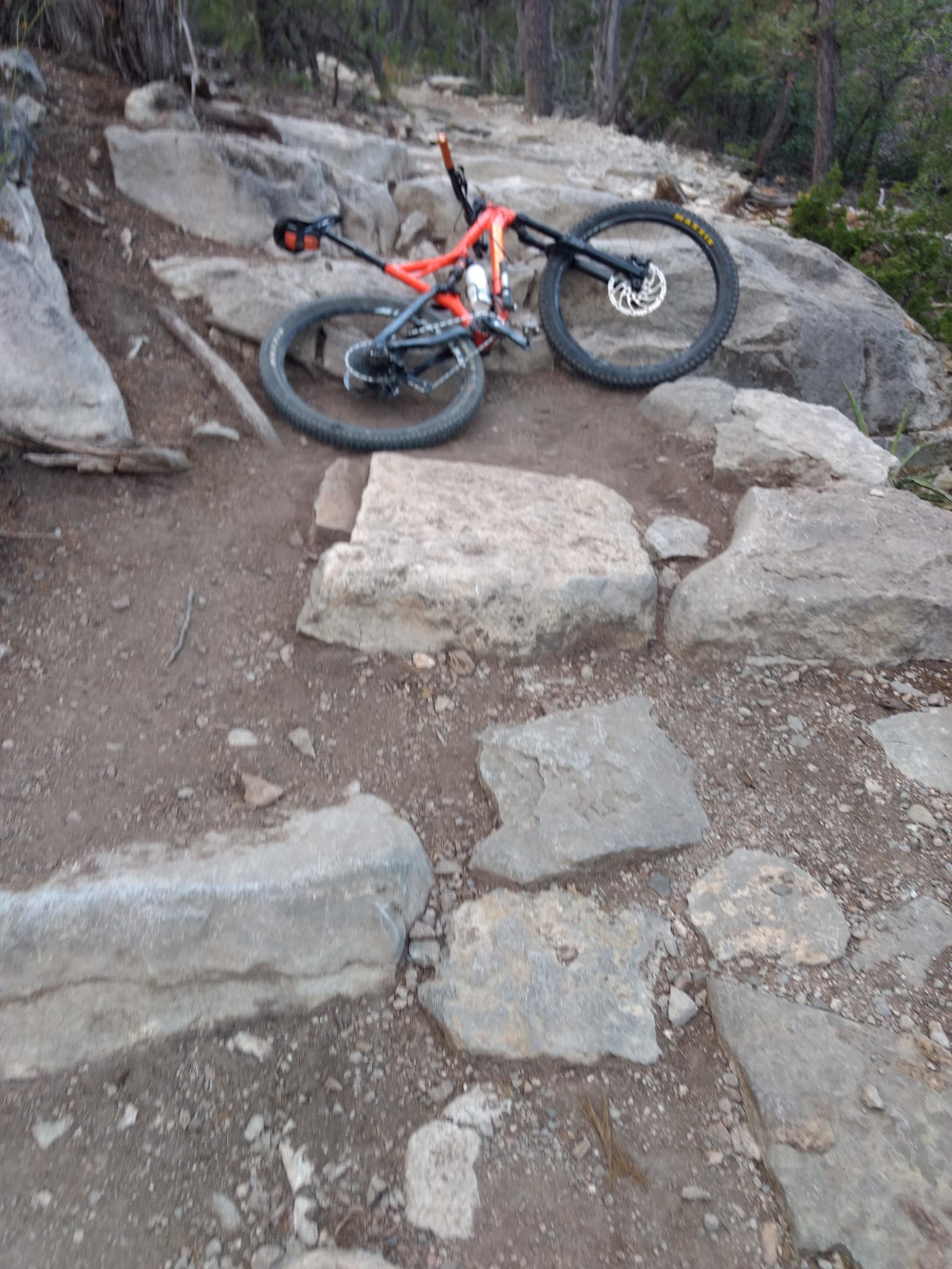 A mountain bike positioned on rocky terrain, surrounded by large stones and dirt. The scene depicts a rugged outdoor trail, suggesting a challenging biking environment. Tunnel Canyon mountain bike trail.