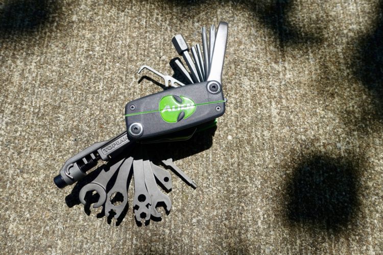 A compact multi-tool featuring various wrenches and screwdrivers, with a green logo, resting on a textured concrete surface.