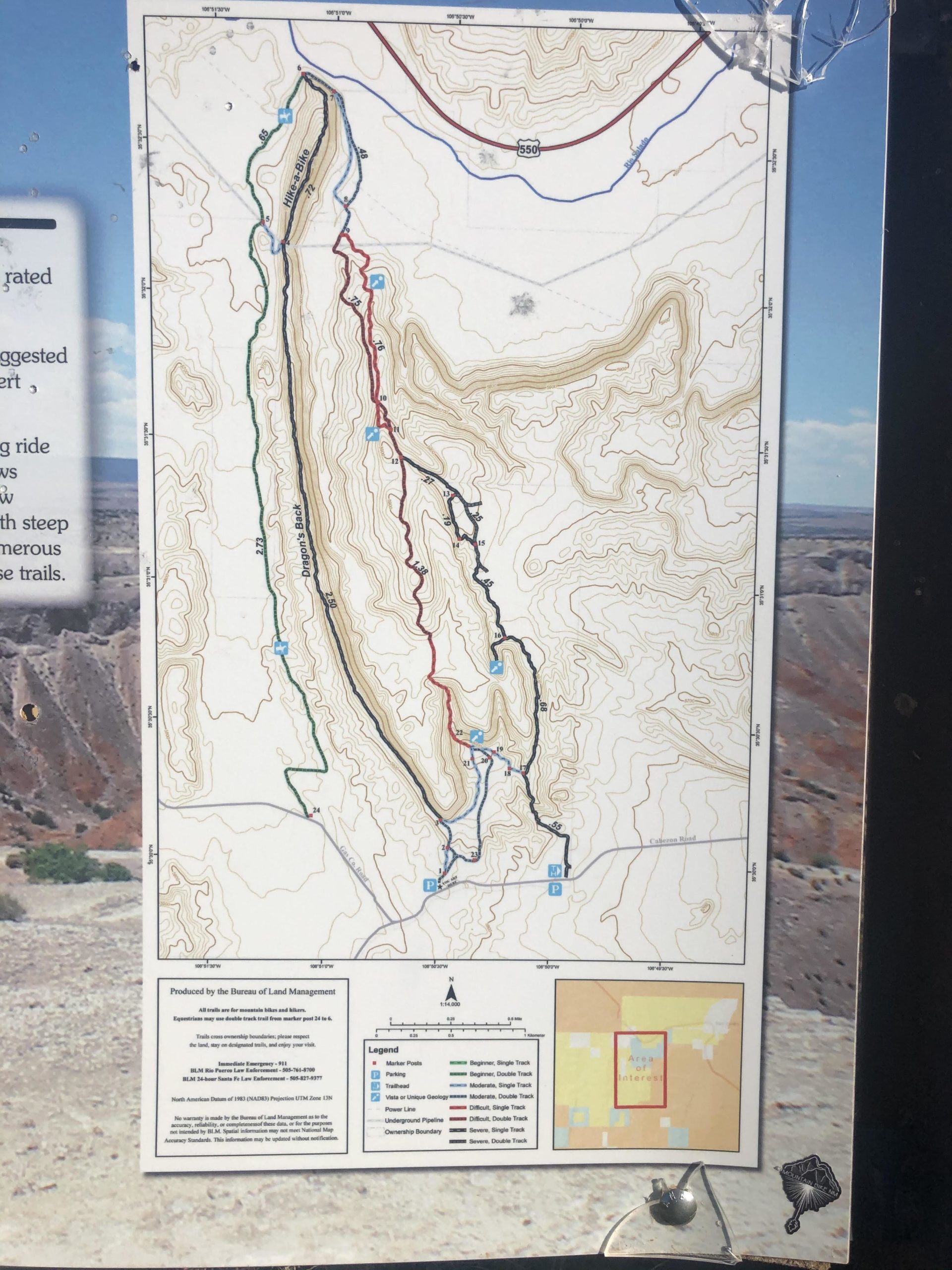 A topographic map displaying various trails and roads in a mountainous area, with contour lines illustrating elevation changes. The map includes key features such as parking areas and trail markers, and features a color-coded legend indicating different types of paths. The background shows rugged terrain typical of the region. White Ridge Bike Trails mountain bike trail.