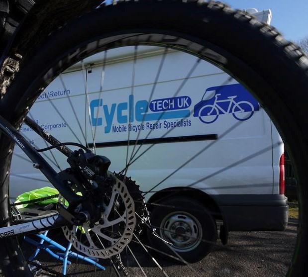 View of a bicycle wheel with a disc brake in the foreground, and a van with the logo "Cycle Tech UK" and the text "Mobile Bicycle Repair Specialists" in the background.