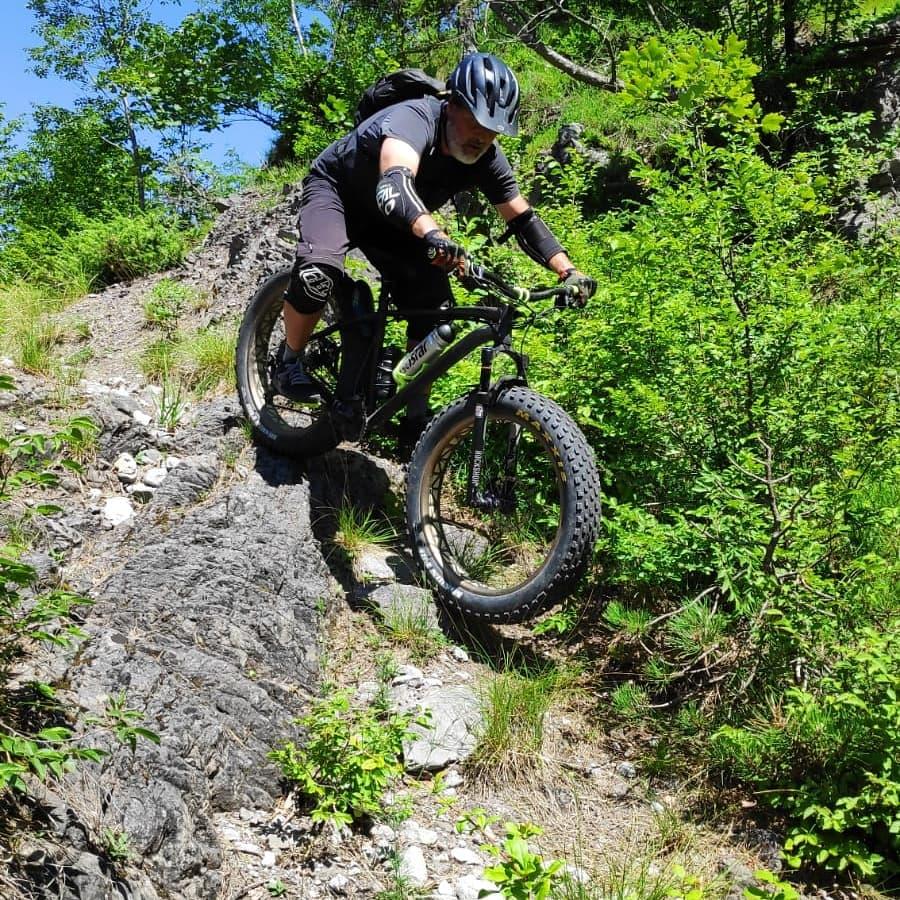 Rocky Mountain Pipeline: A cyclist navigating a rocky trail on a fat tire mountain bike, wearing protective gear, surrounded by greenery on a sunny day.