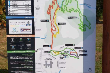 Map of the Oz Trails in Springdale, featuring various biking and hiking trails, with color-coded difficulty levels. The map includes a legend, nearby landmarks, and trail descriptions. The layout shows trails winding through natural landscape, with icons indicating features like parking and rest areas. Bayyari Park mountain bike trail.