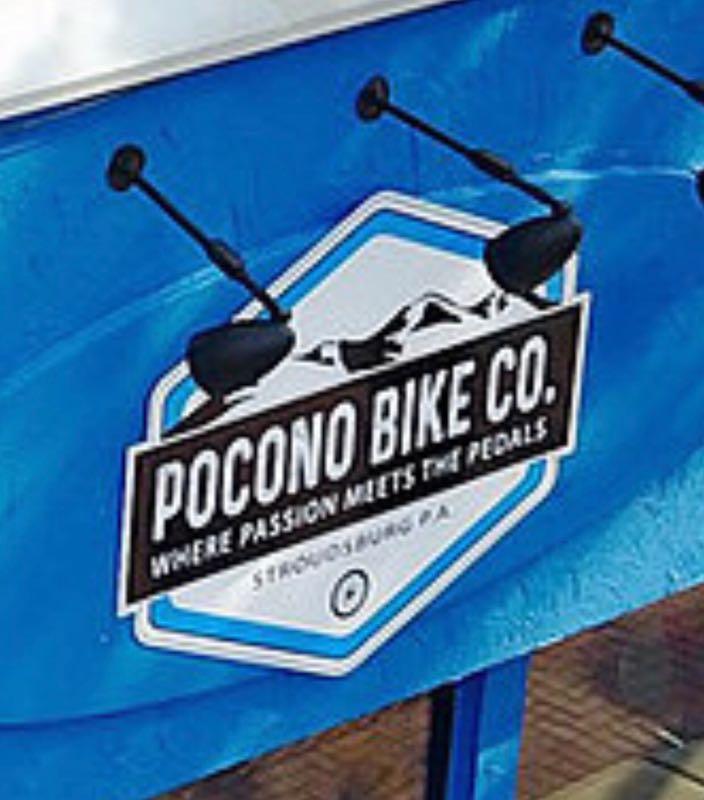 Logo of Pocono Bike Co. featuring the text "Where Passion Meets the Pedals" with a mountainous design background, set against a blue wall. The location is Stroudsburg, PA.