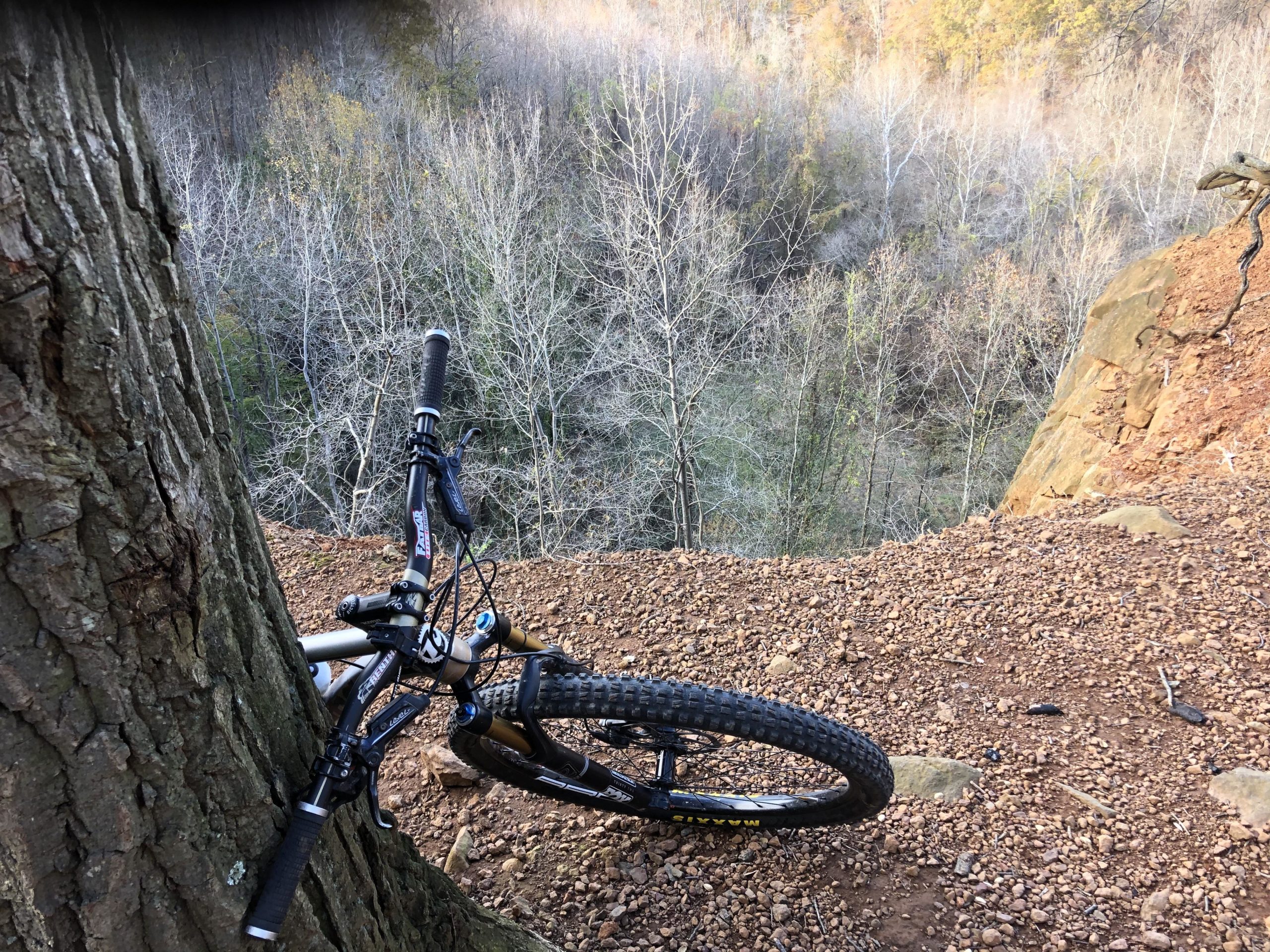 A mountain bike leaning against a tree on the edge of a steep, rocky slope, overlooking a landscape of bare trees and a valley. Gunpowder Falls State Park mountain bike trail.