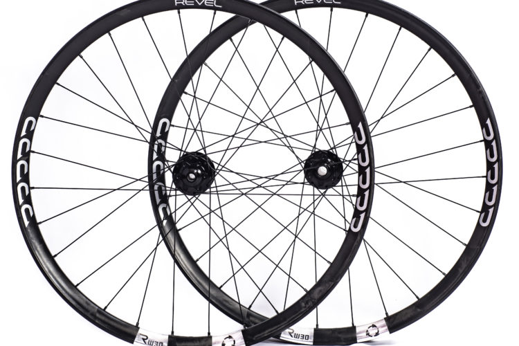 Two black bicycle wheels with multiple spokes, featuring 'REVEL' branding on the rims and 'RW30' markings on the hubs, positioned slightly overlapping against a white background.