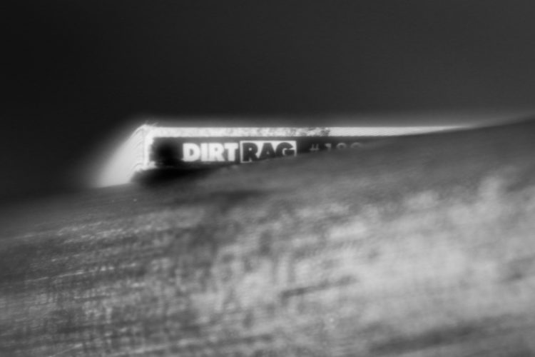 Close-up of a magazine titled "Dirt Rag," partially obscured by a textured wooden surface, presented in black and white.