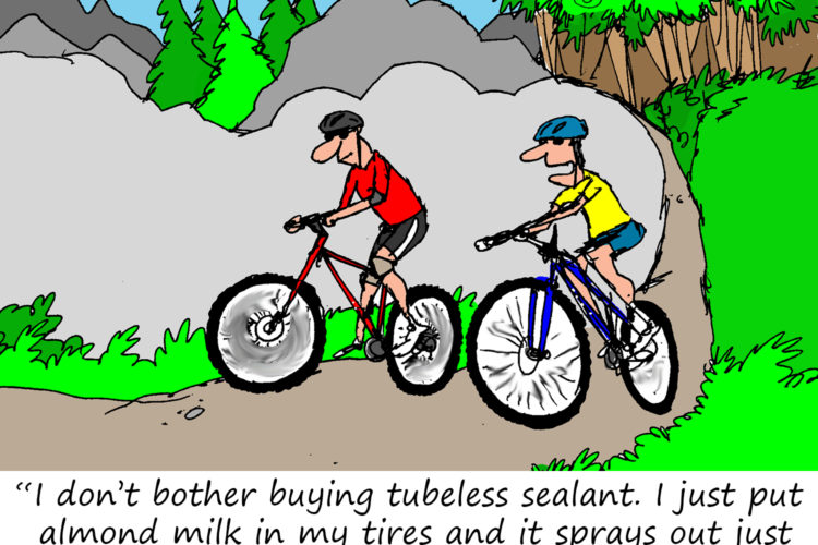 A cartoon featuring two cyclists riding on a dirt trail surrounded by trees and mountains. One cyclist, wearing a red jersey, is making a humorous comment about using almond milk in his tires instead of tubeless sealant. The other cyclist, dressed in yellow, listens. The scene conveys a light-hearted take on biking maintenance.