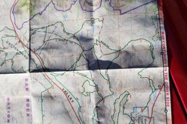 Map of Red Rock Canyon National Conservation Area, featuring trails, topographic details, and key landmarks, partially folded with bright lighting casting shadows. Blue Diamond mountain bike trail.