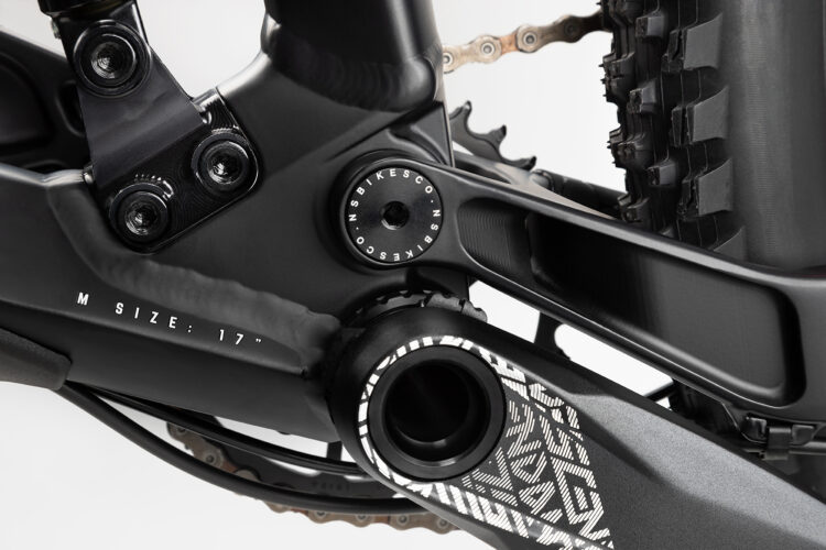 Close-up view of a mountain bike's bottom bracket area, featuring a black frame with visible components such as bolts and a size indicator marked "M SIZE: 17". The image highlights the intricate design of the bike's frame and the texture of the crank arm, showcasing the mechanical details and craftsmanship.