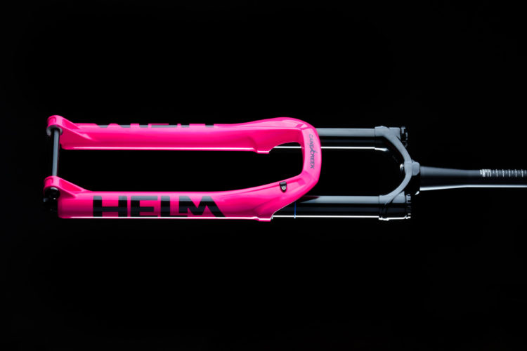 A bright pink mountain bike fork with black accents and the word "HELM" prominently displayed, against a black background.