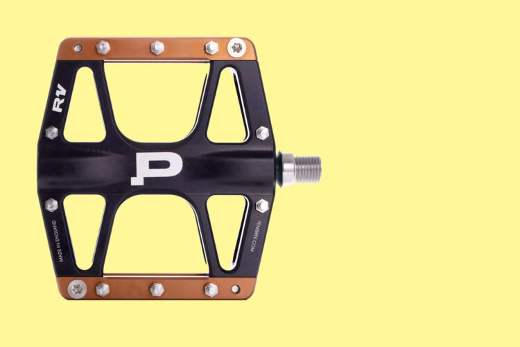 Black bike pedal with a copper-colored top edge, featuring a large "P" logo and multiple screws, set against a light yellow background.