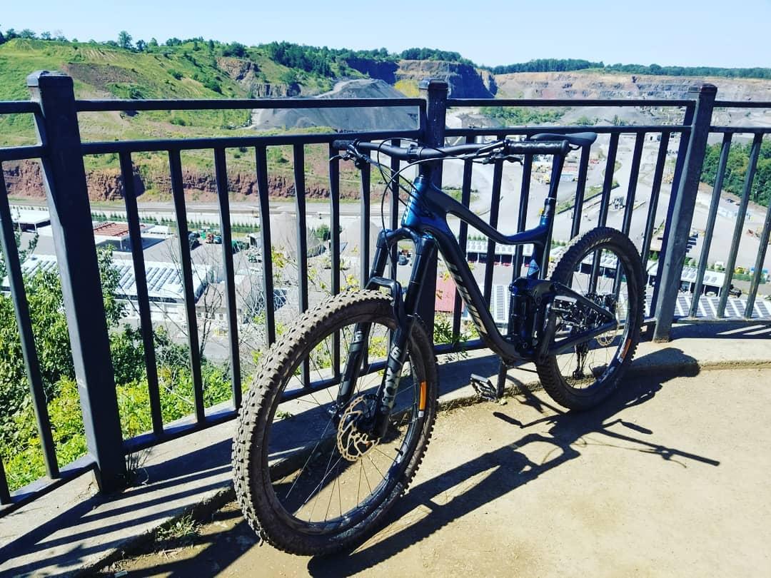 Giant Trance Advanced: A black mountain bike parked beside a railing, overlooking a scenic view of a quarry and green hills under a clear blue sky.