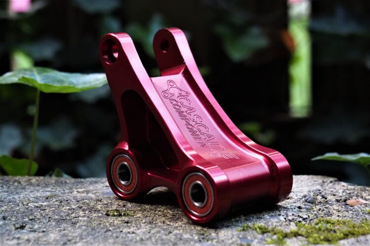 Alt text: A close-up image of a red aluminum bike component, showcasing its sleek design and bearing edges, set against a blurred background of greenery.