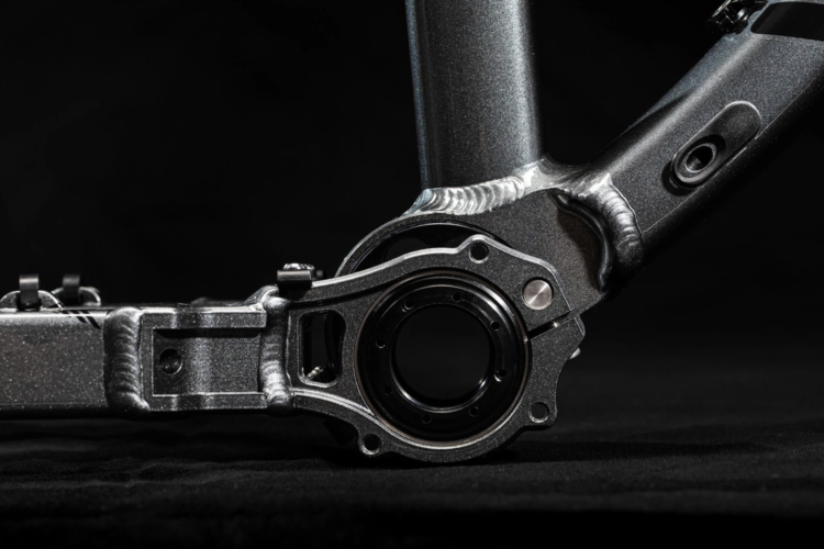 Close-up view of a bicycle bottom bracket assembly, showcasing a metallic frame component with detailed welding and threading, set against a dark background.