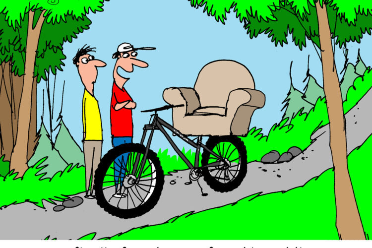 A cartoon depicting two men standing beside a mountain bike with a cushioned armchair attached as the seat. One man, wearing a red shirt and a baseball cap, is smiling, while the other, in a yellow shirt, looks on with an amused expression. The background features a scenic trail surrounded by trees and mountains. The caption reads, "I finally found a comfortable saddle."