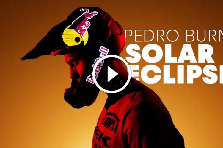 A profile view of a person wearing a black helmet with a Red Bull logo, set against a warm orange background. The text "Pedro Burns" and "Solar Eclipse" is prominently displayed. A play button is positioned in the center of the image, indicating video content.