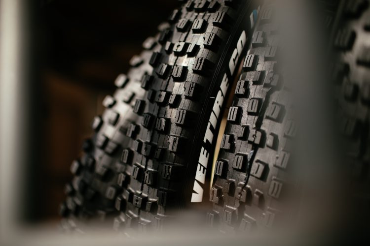 Close-up view of two mountain bike tires with textured tread patterns, featuring the brand logo "VEE TIRE CO" visible on the sidewall. The image showcases the details of the tire's surface and design.