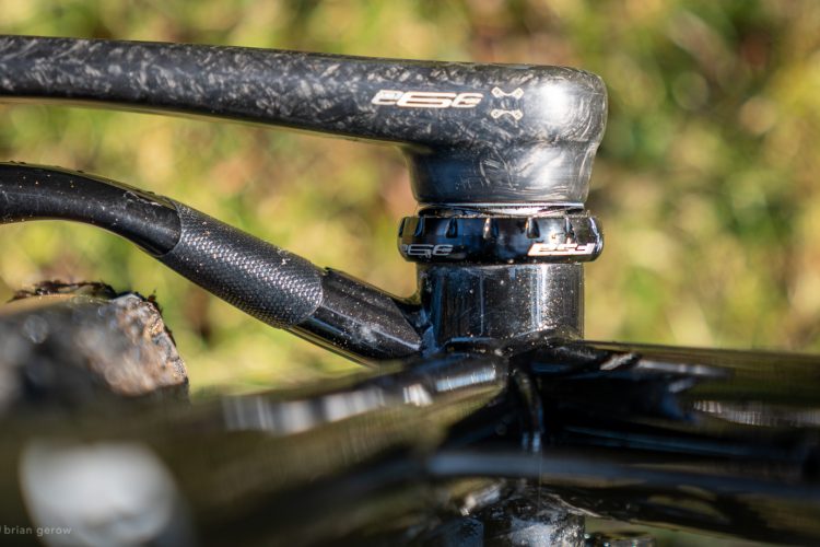 Close-up of a bike's head tube and stem assembly, featuring a carbon fiber handlebar and ESE branding on the components, set against a blurred green background.