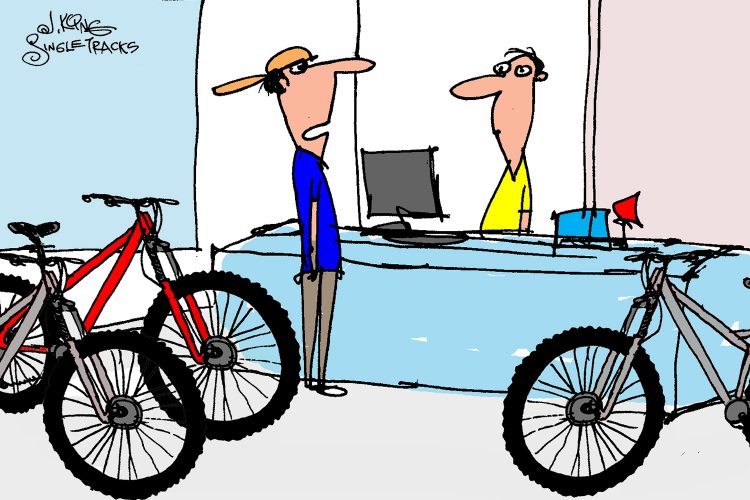A cartoon depicting a bicycle shop interior. On the left, there are several bikes with prominent tires. A customer in a blue shirt and hat stands at the counter, looking at a shop employee, who is wearing a yellow shirt and standing behind the register. The customer expresses enthusiasm about wanting 26x1.95 tires.
