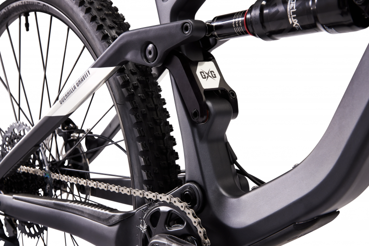 Close-up image of a mountain bike's rear suspension and drivetrain components, showcasing the bike's frame, shock absorber, chain, and tire with a focus on the intricate design and engineering of the parts.