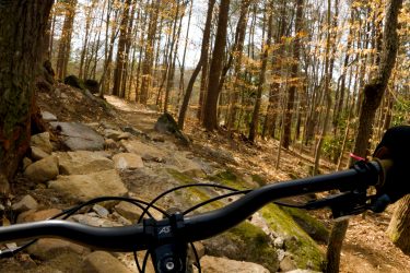 Mountain biking view from the handlebars on a rocky trail surrounded by trees with autumn leaves. Moontower mountain bike trail.