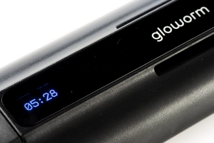 A close-up image of a black Glowworm device featuring a digital display that shows the time as 05:28. The device has a sleek design with a matte finish and a logo prominently displayed on the front.