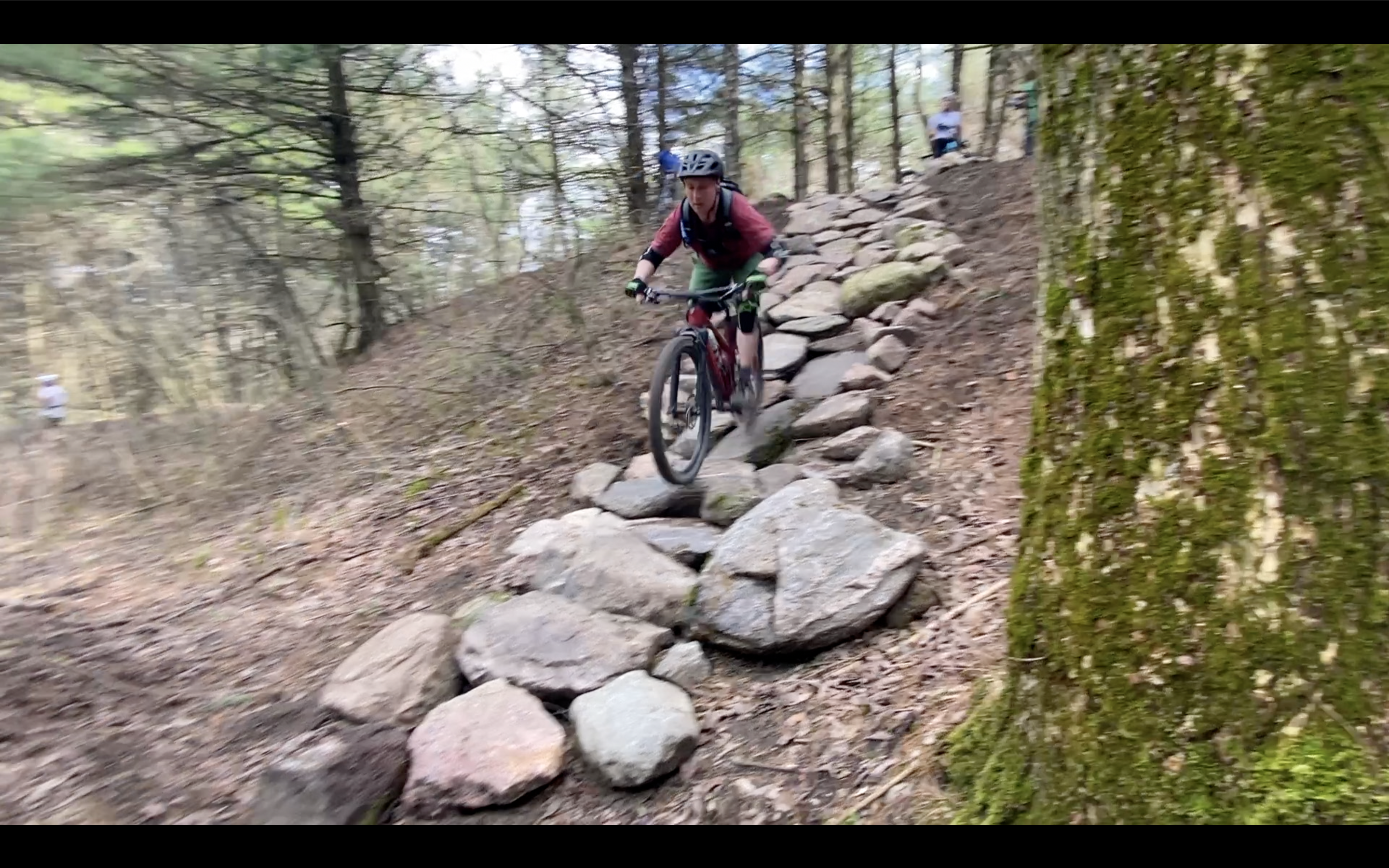 A mountain biker navigating a rocky trail through a wooded area, displaying skill and agility on a challenging section of the path. Rock Garden mountain bike trail.