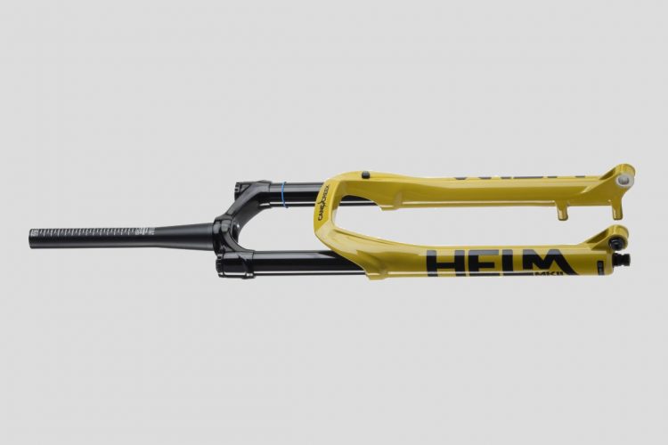Image of a mountain bike fork with a vibrant yellow and black design, featuring the word "HELM" prominently displayed. The fork has a sleek, modern look, showing suspension components and a straight steerer tube. The background is neutral to highlight the product.