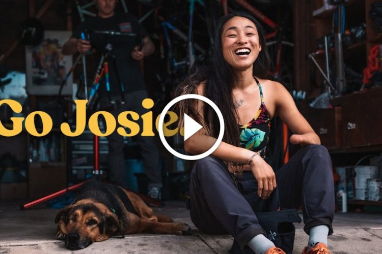 A woman smiling while sitting on the ground in a garage, next to a relaxed dog. The background features bicycle parts and tools, suggesting a workshop environment. The text "Go Josie" is prominently displayed.