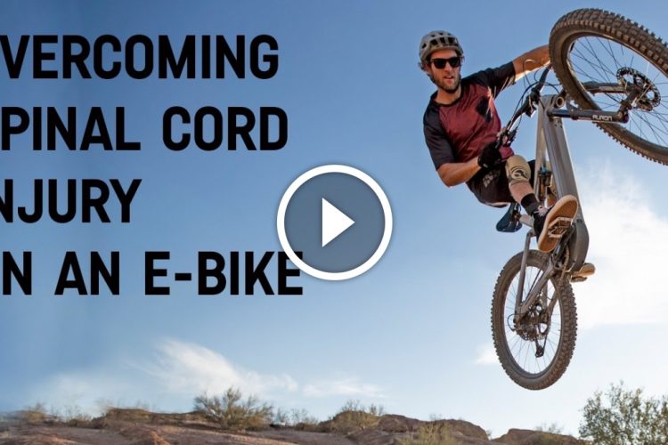 A person performing a stunt on an electric bike in a sunny outdoor setting, with text overlay reading "Overcoming Spinal Cord Injury on an E-Bike." A play button icon is displayed in the center of the image, suggesting that it is a video.