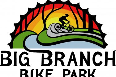 Logo for Big Branch Bike Park featuring a silhouette of a mountain biker riding on a stylized trail, with a colorful sunset and abstract landscape elements in the background. The name "BIG BRANCH BIKE PARK" is prominently displayed at the bottom in bold letters. Big Branch Bike Park mountain bike trail.