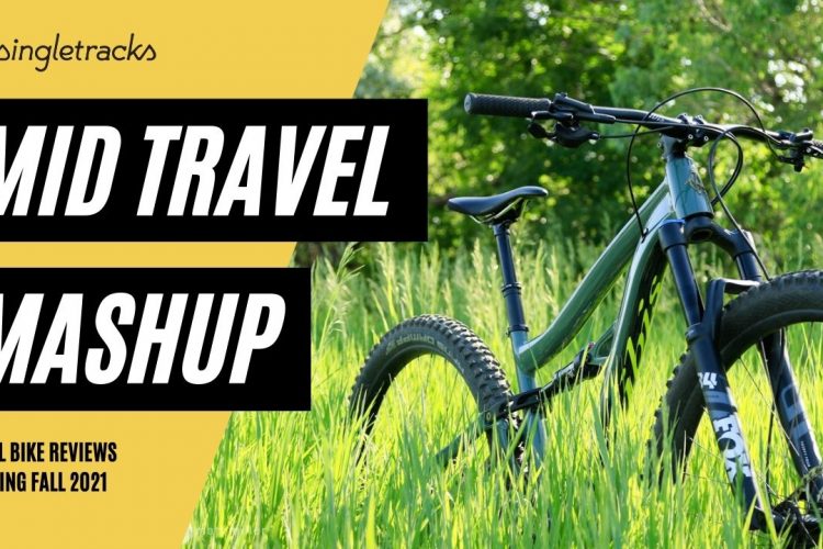 Alt text: A mountain bike is positioned in a field of tall green grass, with vibrant greenery in the background. The image features bold text reading "MID TRAVEL MASHUP" and "TRAIL BIKE REVIEWS COMING FALL 2021."