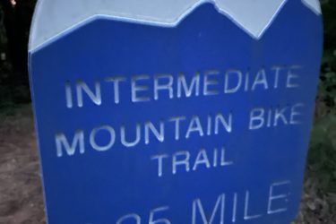 Sign for an intermediate mountain bike trail indicating a distance of 2.25 miles, featuring a blue background with white text and mountain graphic. South Rockdale Community Park mountain bike trail.