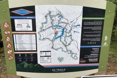 Map of the Little Sugar Trail System in Northwest Arkansas, displaying various trails, their lengths, difficulty levels, and etiquette guidelines for trail users. The map includes sponsor logos, emergency contact information, and notes on trail usage and safety. Little Sugar Creek mountain bike trail.