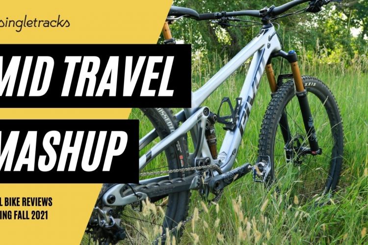 A mountain bike positioned in a grassy outdoor setting, featuring a detailed view of its frame, wheels, and suspension components. The image includes promotional text for "Mid Travel Mashup," highlighting upcoming trail bike reviews expected in Fall 2021, set against a vibrant yellow background.