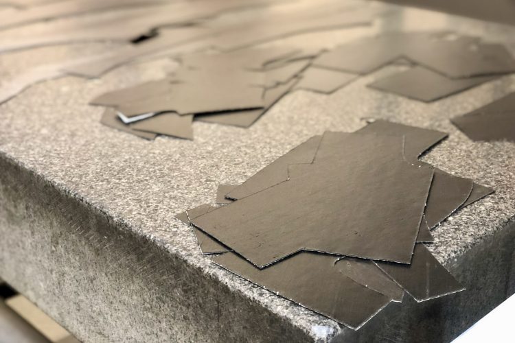 A close-up view of a surface covered with several black cut-out shapes, resting on a textured gray table. The shapes are irregular and vary in size, indicating a crafting or design process.