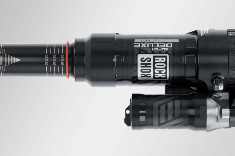 Alt text: "A top-down view of a RockShox Super Deluxe Ultimate mountain bike shock absorber, featuring a black cylindrical body with measurement markings and an adjustable air chamber."