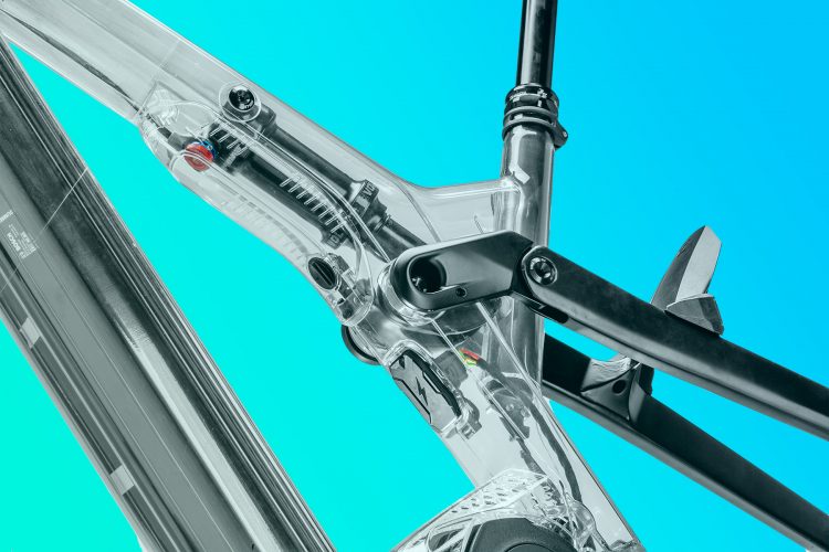 Close-up view of a transparent bike frame showcasing its intricate suspension system and components, set against a vibrant turquoise background.