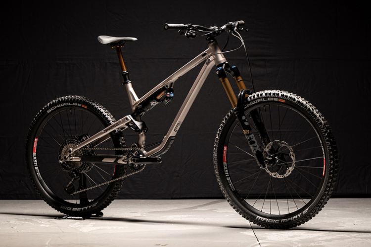 A sleek, modern mountain bike with a lightweight aluminum frame, featuring front and rear suspension. The bike is positioned on a light-colored surface against a dark backdrop. It has high-quality components, including Schwalbe tires and a precision drivetrain. The handlebars and seat are angled for optimal performance.