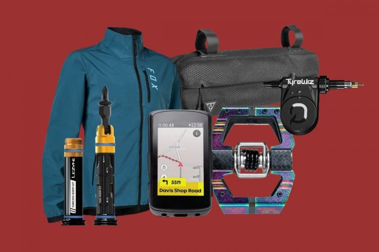 A collection of cycling gear on a red background, including a blue jacket, a tire repair kit, a multi-tool, a bike GPS device displaying a map, a colorful pedal, and a tire inflator.