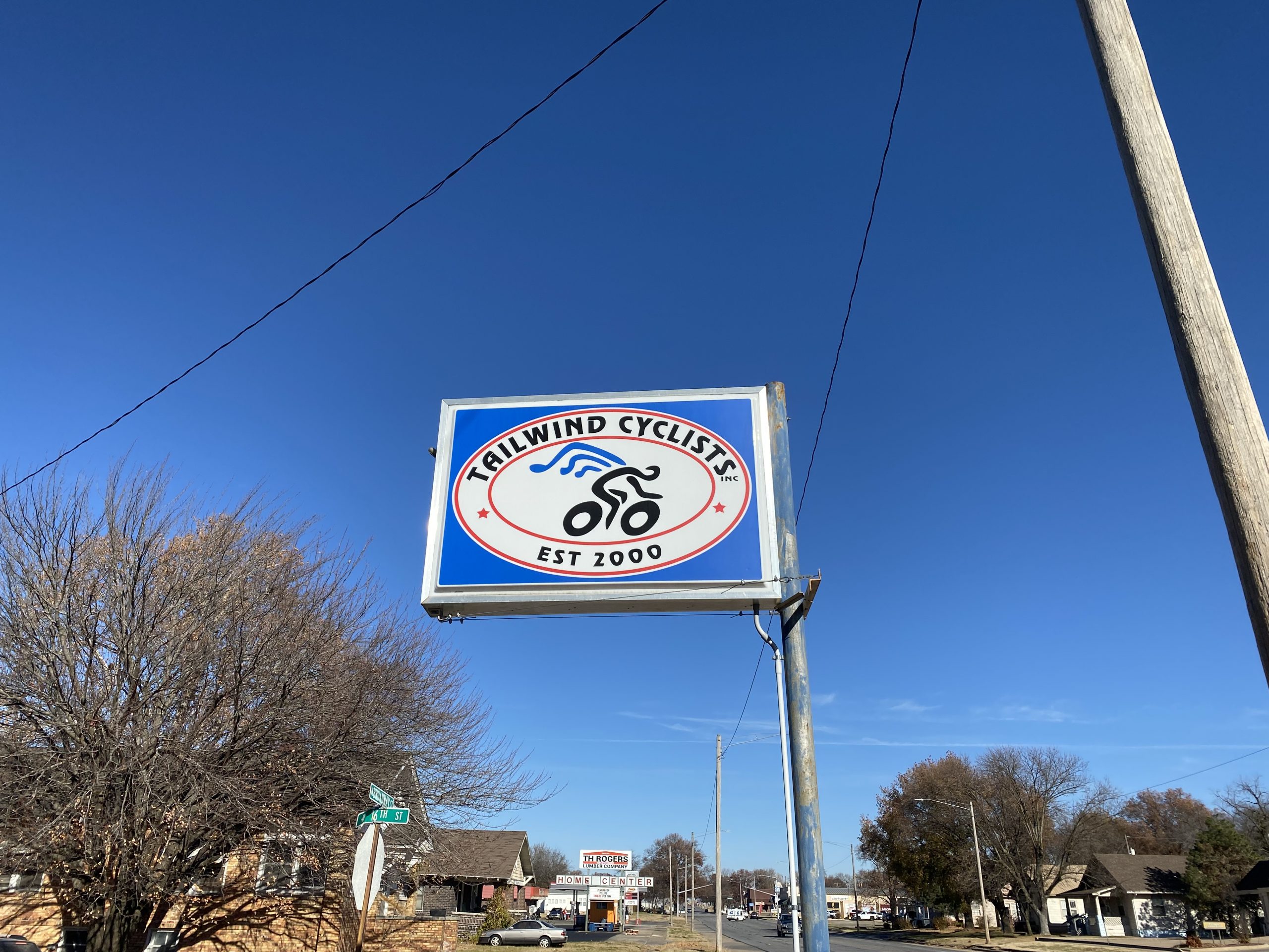 Sign for Trailwind Cyclists, established in 2000, featuring a bicycle graphic and blue skies in the background.