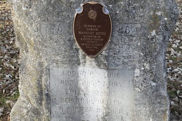 A weathered stone monument honoring Sarah Handley Keyes, who is recognized as the daughter of Revolutionary War patriot Arthur Barrett. The plaque includes the text "In honor of Sarah Handley Keyes" and additional inscriptions commemorating her legacy. Surrounding the monument are trees and fallen leaves, indicating a natural outdoor setting. Alcove Springs mountain bike trail.