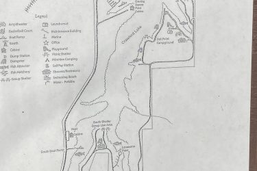 Map of a state park detailing various facilities and features, including cabins, campgrounds, trails, and recreational areas like a swimming beach, playground, and picnic shelters. Key locations such as the office, boat ramp, and restrooms are marked, along with a legend for navigating the area. Drywood Creek Trail mountain bike trail.